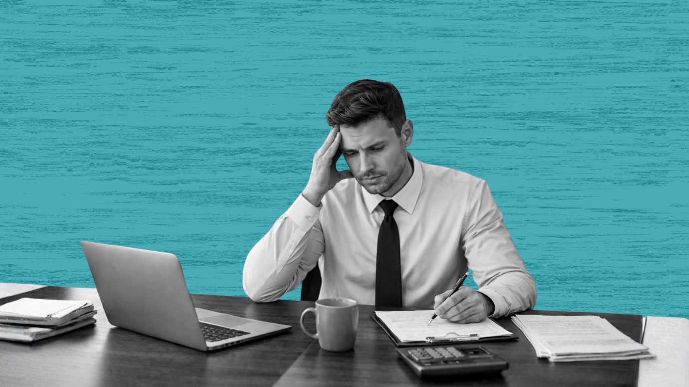 Male attorney sitting in front of his laptop with a legal pad, coffee cup and calculator, holding his head.