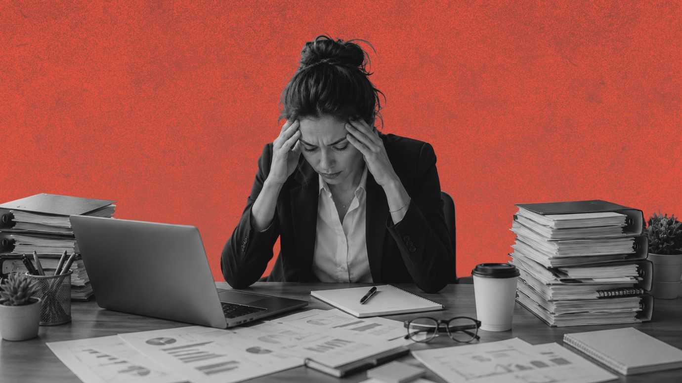 A female attorney holding her head sitting at a cluttered desk. 