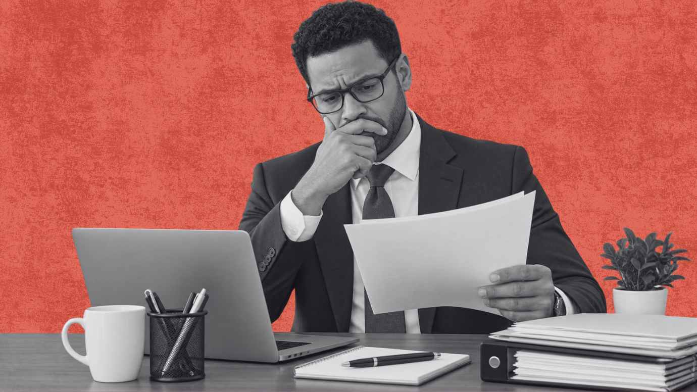Male attorney looking with concern at paperwork in hand at his desk. 